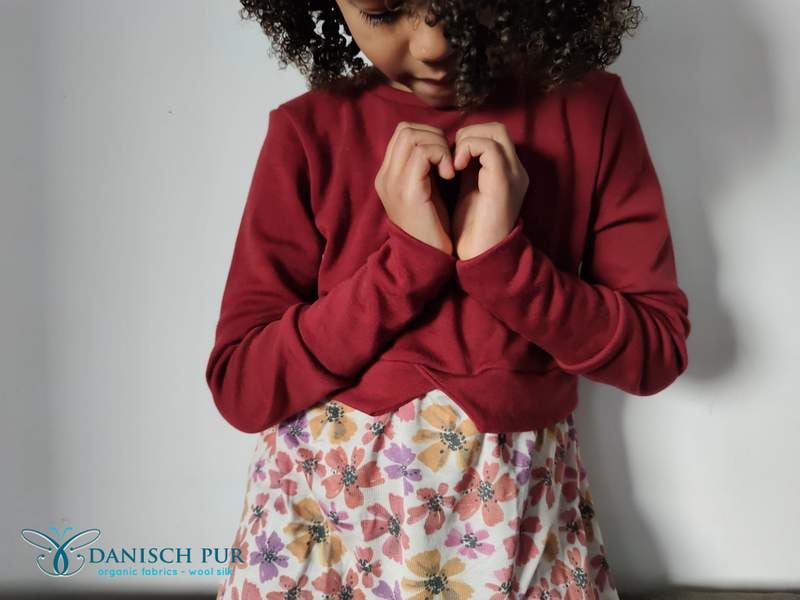 Kind in Wollstoffen formt ein Herz mit den Händen