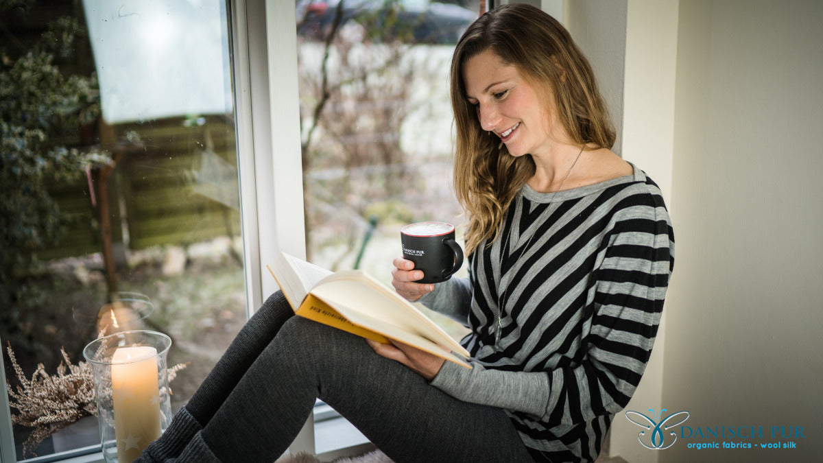 Frau, sitzend auf Fensterbank in gestreiftem Wolljersey Pullover am Fenster mit Kaffee und Buch.